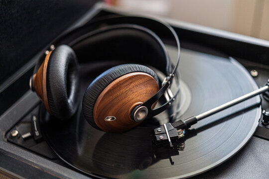 Vintage headphones made of wood are on a black vinyl in a record player