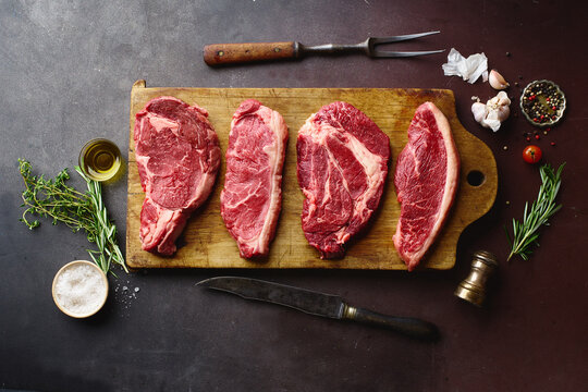 Top view of raw black angus prime beef steaks on wooden cutting board: rib eye, chuck roll, striploin and picanha.