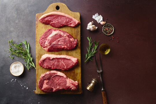 Top view of raw black angus prime beef steaks on wooden cutting board: rib eye, chuck roll, striploin and picanha.