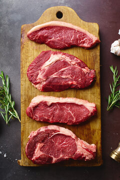 Top view of raw black angus prime beef steaks on wooden cutting board: rib eye, chuck roll, striploin and picanha.