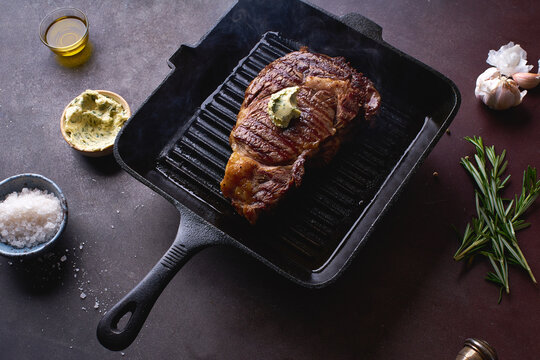 Cooked black angus prime beef ribeye steak on cast iron grilling pan with herbs, butter and spices