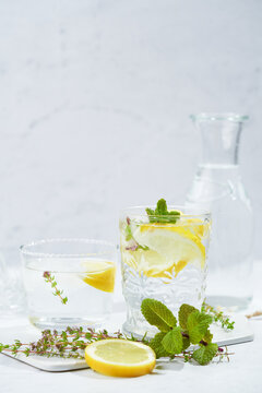 Glasses with refreshing cold thyme and ginger lemonade with slices of lemon and mint leaves served on table in light room