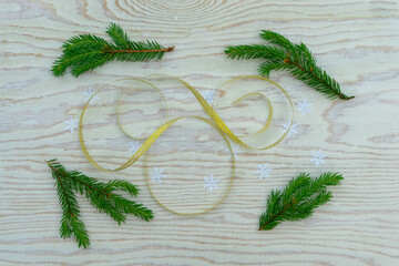Christmas layout with sprigs of spruce and gold ribbon on a wooden background.