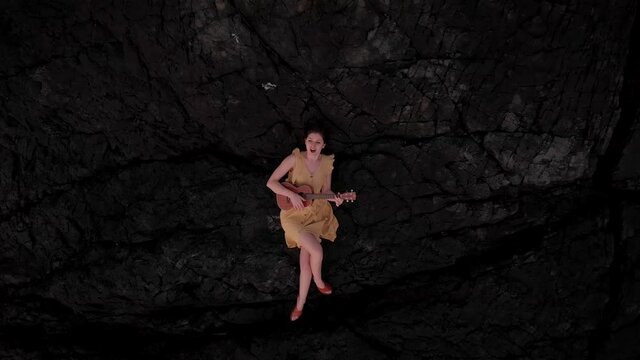 Young attractive brunette woman playing a ukulele by the ocean at sunset. 4k 24fps.