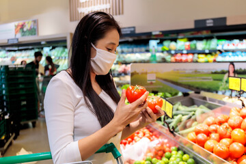 Asian woman wearing protective face mask push and hold shopping cart in supermarket department store. Girl, looking grocery to buy  some food. New normal after covid-19. Family concept.