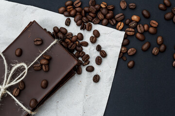 Black chocolate on a black background. Сoffe beans are scattered in the background. Free space in the background. Image of Flat lay. World Chocolate Day.