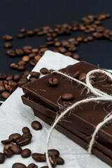 Black chocolate on a black background. Сoffe beans are scattered in the background. Free space in the background. Image of Flat lay. World Chocolate Day.