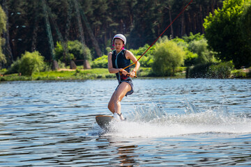 Woman riding wakeboard. Сuts waves and raises splash in a summer lake