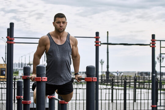 Confident young male athlete exercising on parallel bars against sky