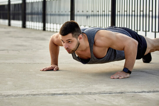Young male athlete practicing push-ups on footpath