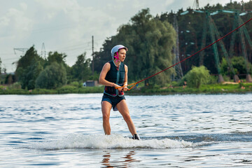 Fototapeta premium Woman riding wakeboard. Cuts waves and raises splash in a summer lake