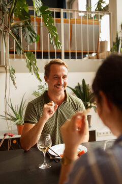 Happy man looking at woman while having food at dining table in house