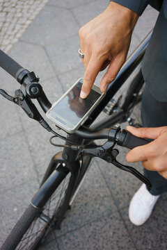 Cropped image of businessman using mobile phone on bicycle handle while standing at street
