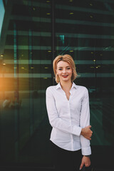Young smiling woman secretary in real estate company is posing, while is waiting customers outside. Beautiful successful businesswoman is looking at camera, while is standing near office building
