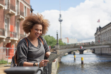Portrait of smiling female tourist standing with map against Fernsehturm, Berlin, Germany