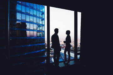 Fototapeta na wymiar Silhouette of a couple of young business people having conversation while standing in hallway company near window, intelligent successful man and woman office workers discuss ideas during break
