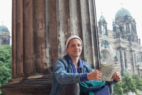 Low angle portrait of young male tourist sitting with map at Altes Museum, Berlin, Germany