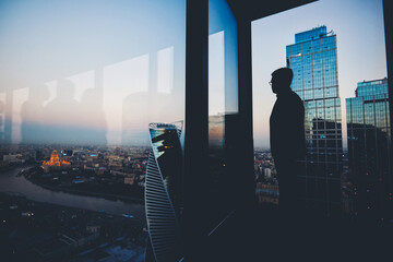 Silhouette of a man financier think about something while standing near office window background...