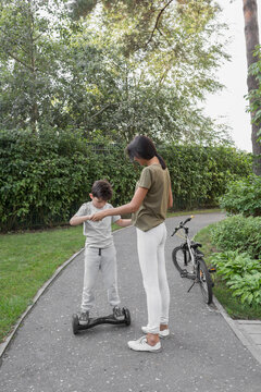 Mother assisting son in using self-balancing board on road against plants