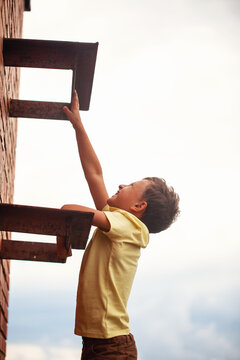teenage boy climbs a brick wall to the roof.