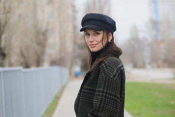 portrait of a brown-haired young girl, wearing a black cap, in a coat, walking alone on city avenue
