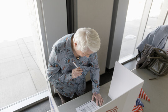 Senior Woman Filling Out Ballot In Voting Booth In Polling Place