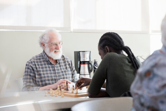 Happy senior man playing chess with young woman in community center