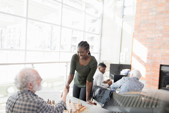 Happy young woman playing chess with senior man in community center