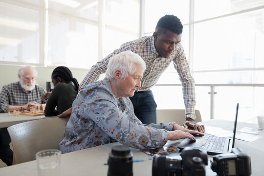 Young man helping senior woman using laptop in community center