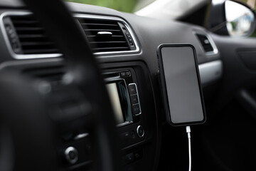 Close-up of modern smartphone with empty screen on charge inside car.