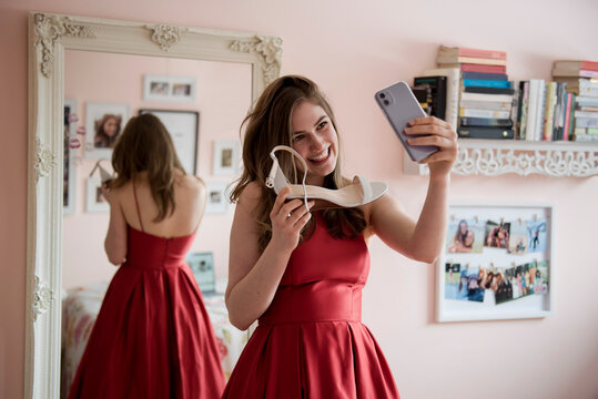 Happy teenage girl in prom dress showing shoes to friends video chat