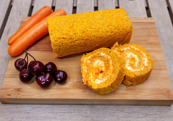 Big vegan roll of carrots, cherries, lactose-free cream and walnuts on a wooden table