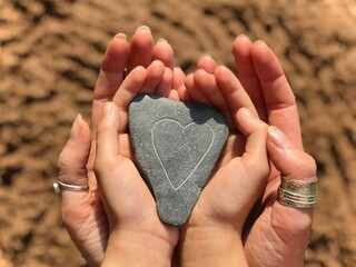 Mother and Daughter holding a love heart stone at the beach on beautiful summers day
