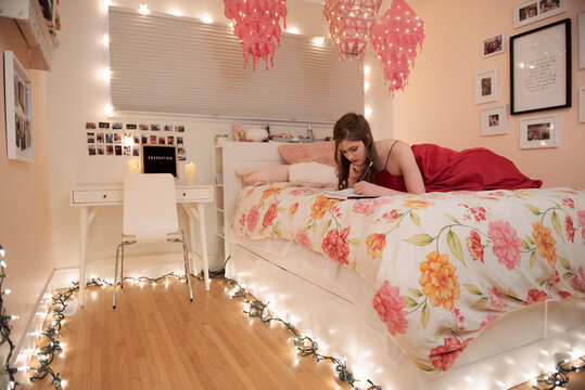 Teenage girl journaling on bed surrounded by string lights
