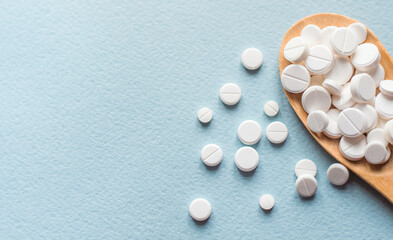 Close-up white pills, tablets in wooden spoon on blue table. Medicine and health concept. pharmaceutics. Top view. Pills and vitamins