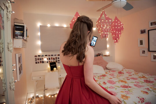 Teenage girl in red graduation dress video chatting with friends