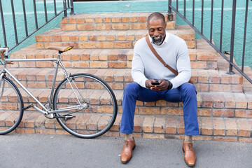 African American man sitting on stairs and using his phone
