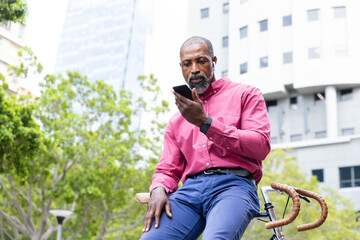African American man sitting on his bike and using his phone 