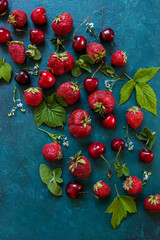 Fresh strawberries and cherries with leaves on a green background