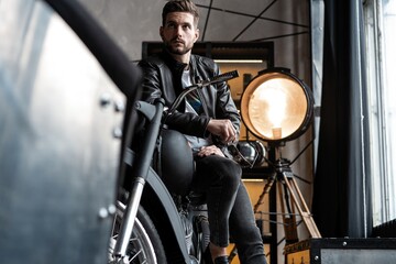 Stylish young man in leather jacket sitting on motorbike.