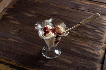 White balls of vanilla ice cream with raspberry jam in a dessert glass with a spoon. Decorated ice cream on an old table made of rough wood. Copyspace flatlay.