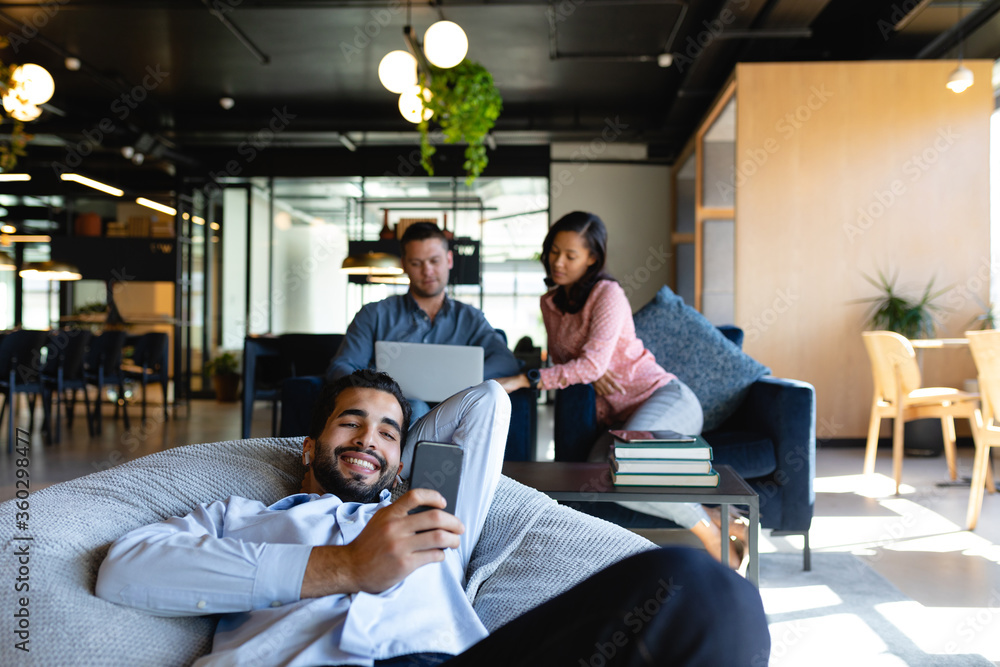 Wall mural caucasian man using his phone on a bean bag in a co working zone