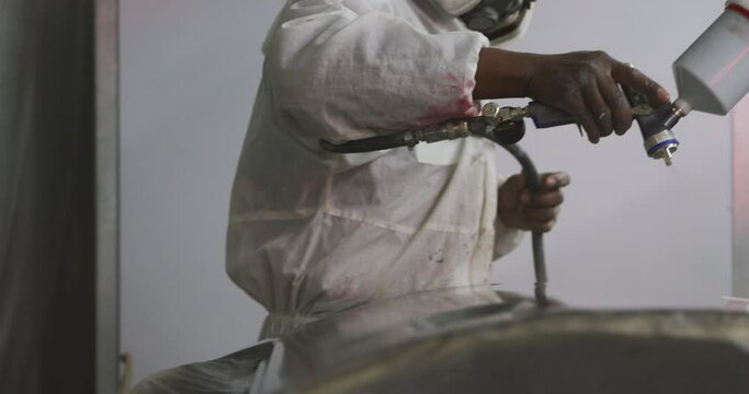 African American male car mechanic with a suit and painting a piece of a car with a spraying gun 