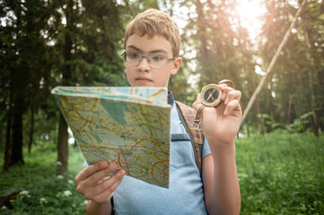 The teenager is hiking. The boy examines the map and looks at the compass.