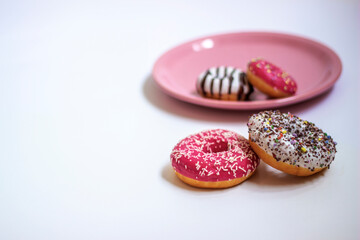 Four glazed donuts isolated on white background. Close up of two colorful donuts on white background and two small donuts on pink plate. Copy space.