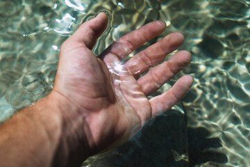 Horizontal photo of a white hand immersing itself in crystal clear river water