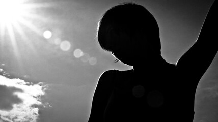 a dark silhouette of a girl with the sun and the sky on the background