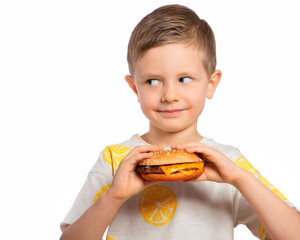 A child eats a cheeseburger. The boy holding the Burger looks around slyly. A beautiful European boy is going to eat fast food. Happy child. Hamburger appetizer. Favorite children's food.