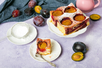 Tasty plum cake with pieces of fruit and powdered sugar on a light background