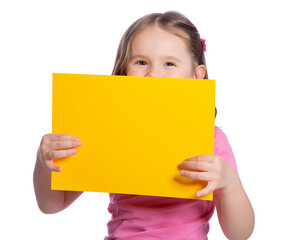 A beautiful European girl of 4 years old holds a yellow sheet of paper on a white background, looks out from behind it and smiles. Space for text, banner, surface for labels and ads.